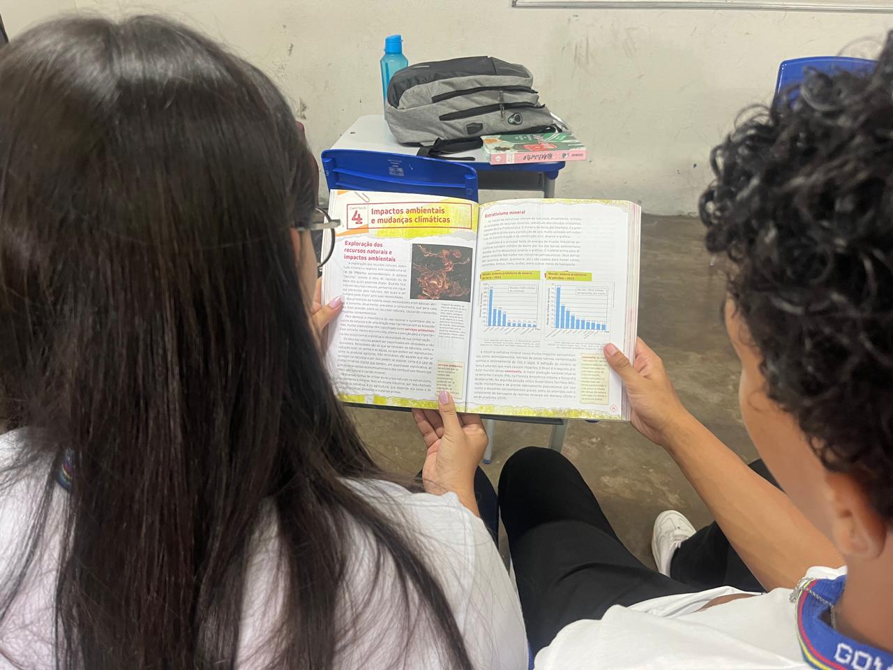 Alunos realizando leitura do livro didático sobre impactos ambientais
