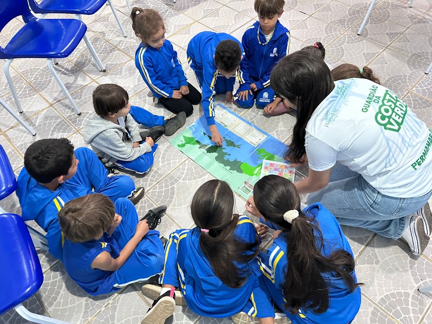 Oficina de mapeamento afetivo realizada com crianças e jovens da comunidade, utilizando mapas ilustrados e adesivos para estimular a participação popular, o pertencimento territorial e a educação climática comunitária.