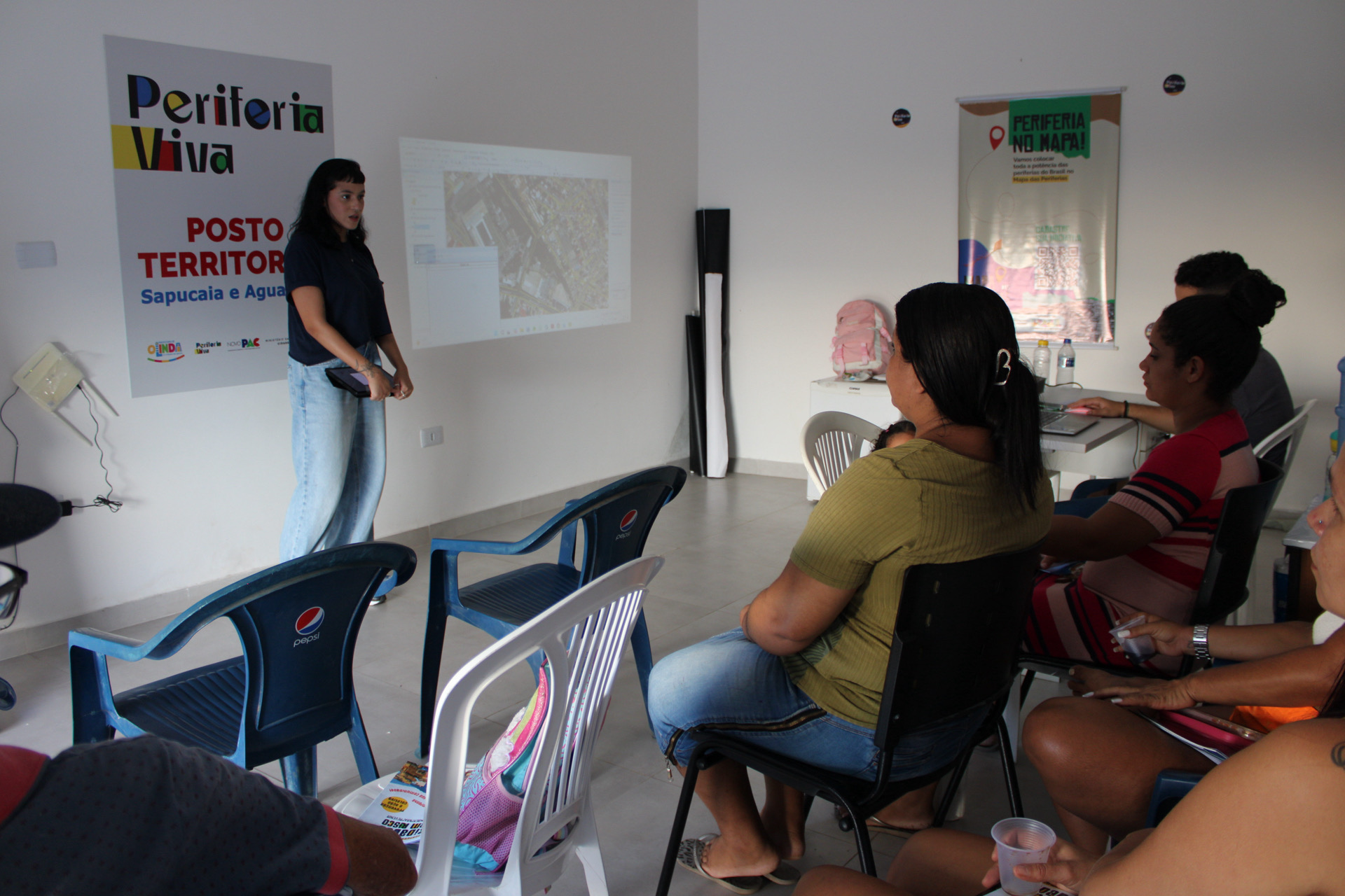 A imagem retrata uma integrante da equipe conduz uma apresentação utilizando projeção de mapas e imagens do território.